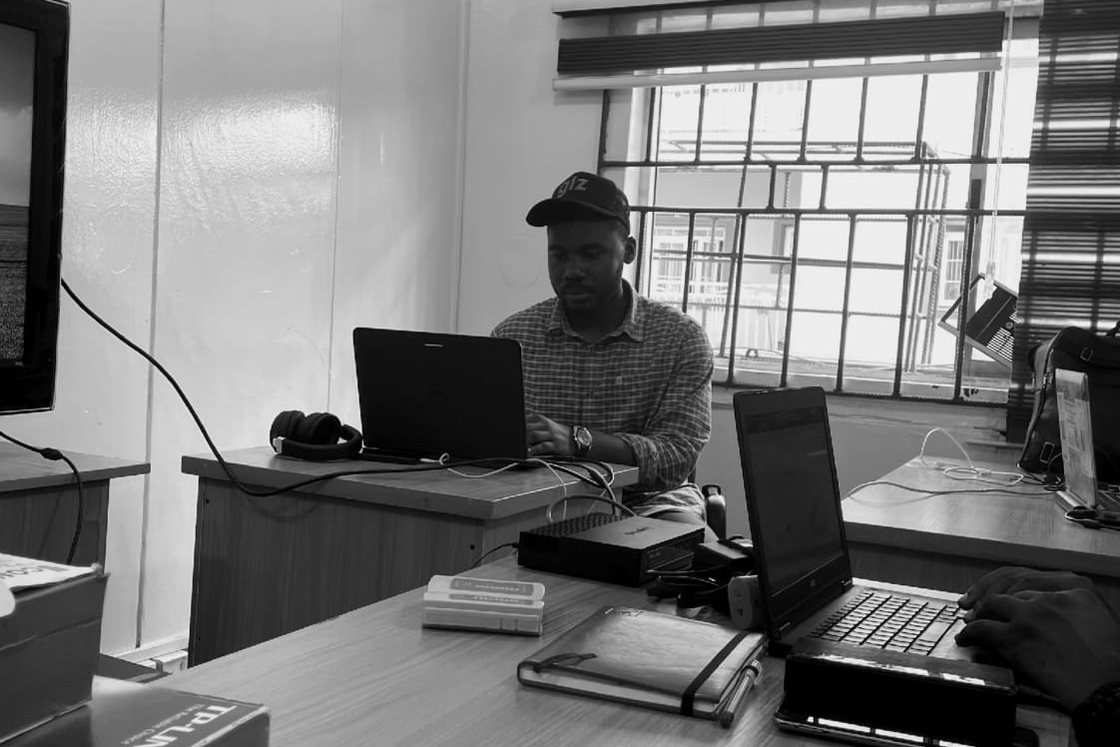 Black-and-white photo of Fortune Johnson building a networking lab with laptops and a TP-Link switch on the desk